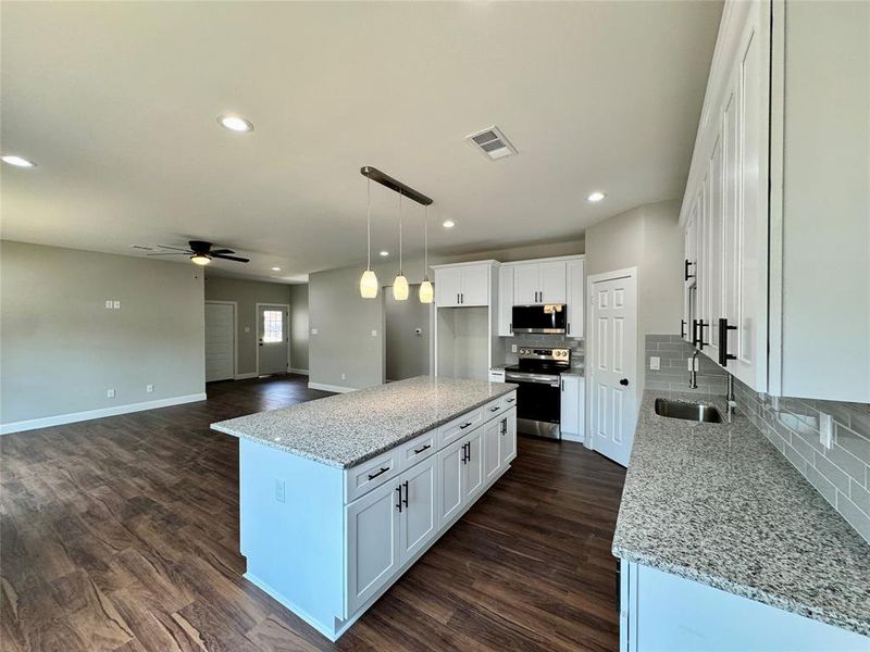 Kitchen featuring tasteful backsplash, stainless steel appliances, ceiling fan, a kitchen island, and dark hardwood / wood-style flooring