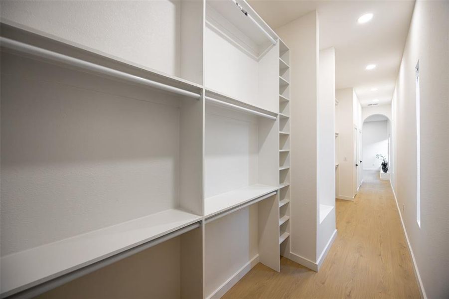 Spacious closet with arched walkways and light wood-style flooring