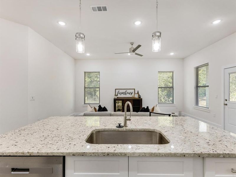 Kitchen featuring pendant lighting, light stone countertops, an island with sink, and recessed lighting