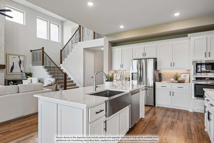 Open-concept kitchen with white cabinets, large island with farmhouse sink, stainless appliances, and hardwood floors overlooking living area and staircase. Open-concept kitchen with white cabinets, large island with farmhouse sink, stainless appliances, and hardwood floors overlooking living area and staircase.