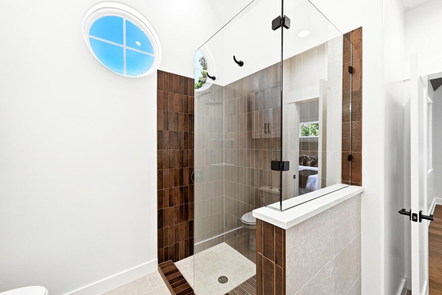 A well-lit primary bathroom features a spacious walk-in shower with clear glass enclosure and a distinctive oval window. A well-lit primary bathroom features a spacious walk-in shower with clear glass enclosure and a distinctive oval window.