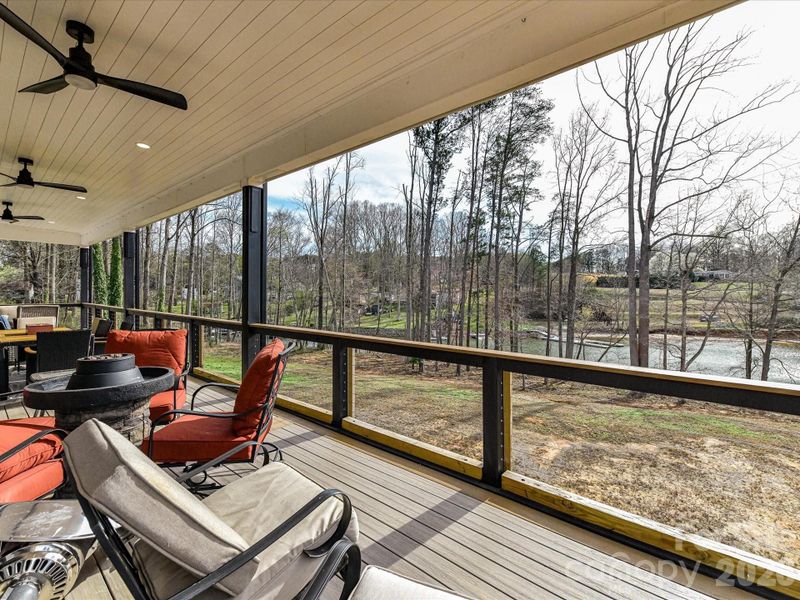 Expansive covered balcony featuring multiple seating areas, ceiling fans, and scenic water views perfect for outdoor entertaining.