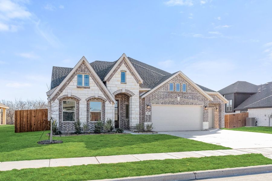 Two-story brick and stone home with arched entry, two-car garage, and green front lawn