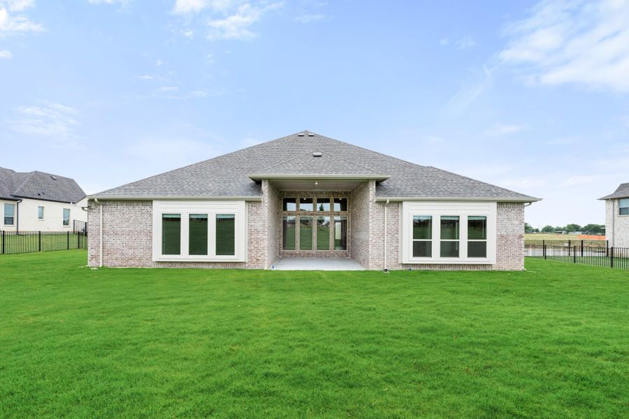 Rear exterior of single-story brick home with covered patio, large windows, and spacious fenced backyard