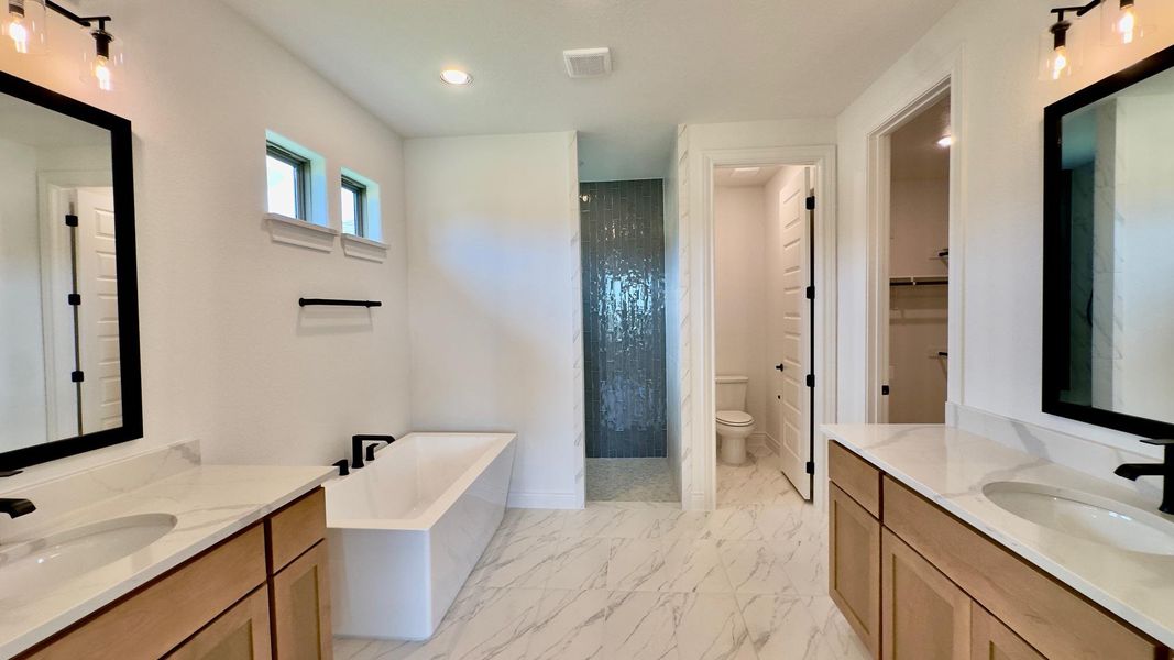 Bathroom featuring two vanities, a freestanding bath, light marble finish floors, walk in shower, and a walk in closet