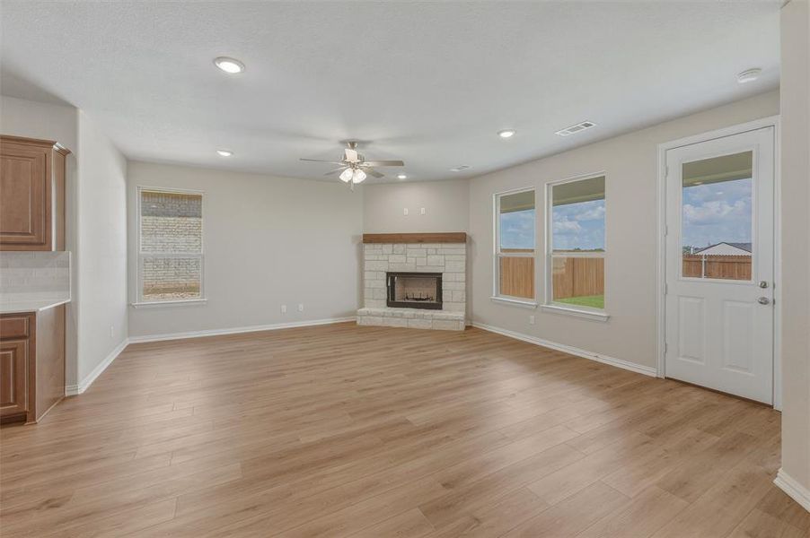 Spacious living area featuring wood-finish flooring, a corner stone fireplace with a wood mantle, recessed lighting, and a ceiling fan Spacious living area featuring wood-finish flooring, a corner stone fireplace with a wood mantle, recessed lighting, and a ceiling fan