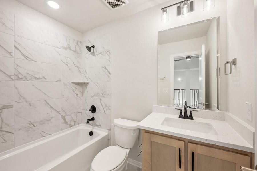 Bathroom with marble-tiled tub and shower, wood vanity with quartz countertop, and black fixtures