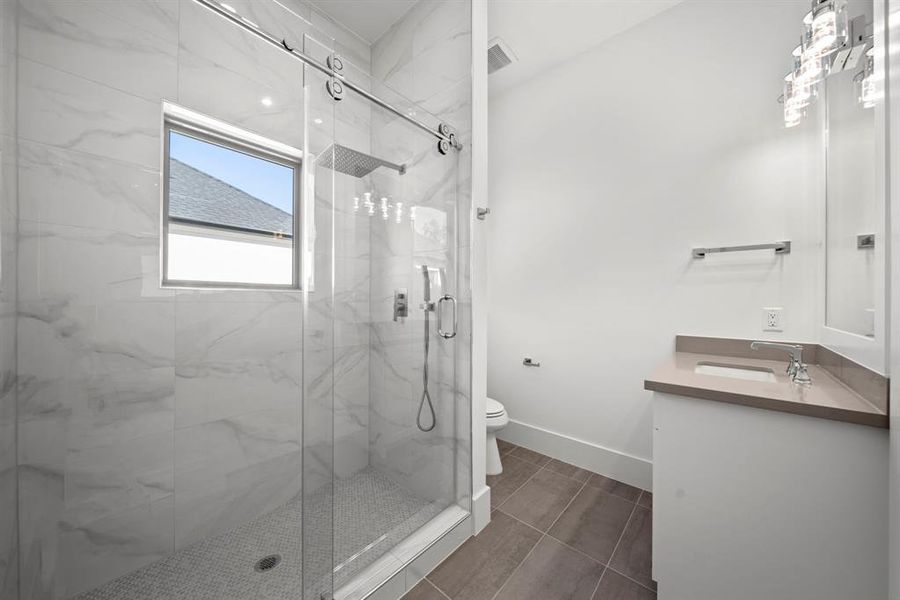 This modern Second bathroom features a sleek design with a frameless glass shower, adorned with marble-inspired tile and a rainfall showerhead for a luxurious experience. The quartz countertop vanity provides ample space, while the contemporary light fixtures add a touch of elegance. With its clean lines and thoughtful layout, this bathroom combines functionality with style, offering a comfortable and sophisticated retreat