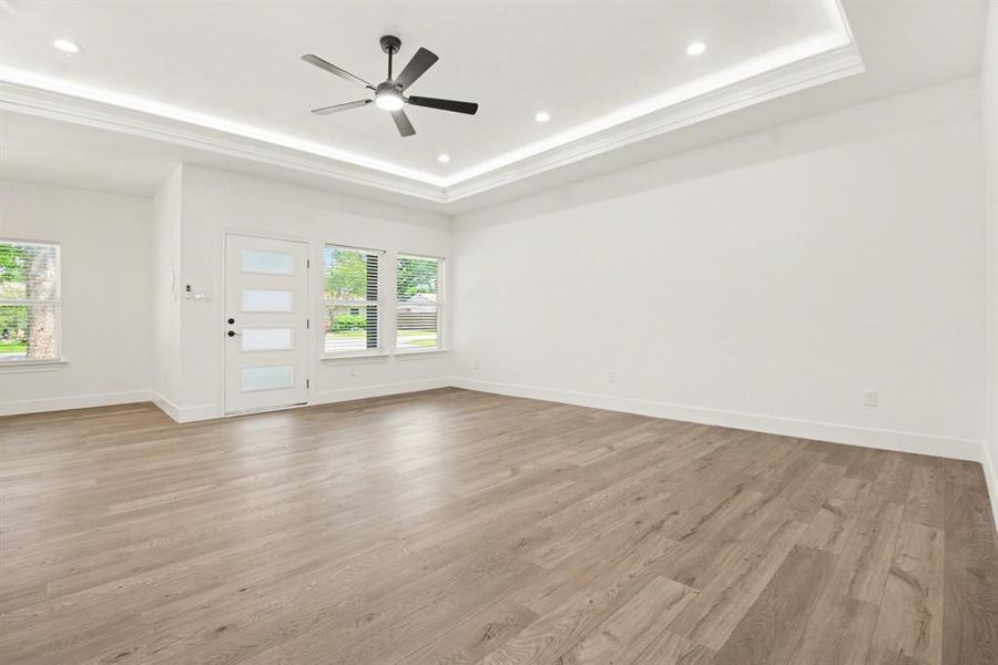 This spacious room features light-toned wood flooring, a modern ceiling fan with lighting, and recessed ceiling lights