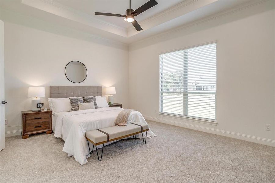 Bedroom featuring ceiling fan, crown molding, a tray ceiling, and light colored carpet