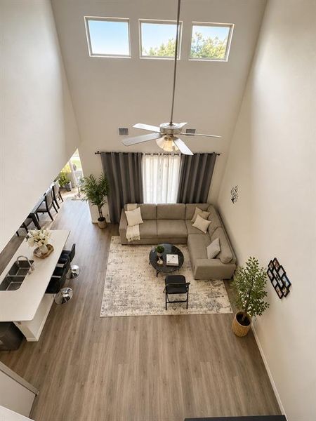 Open-concept living space featuring high ceilings, wood-finish flooring, a contemporary ceiling fan, and multiple upper windows Open-concept living space featuring high ceilings, wood-finish flooring, a contemporary ceiling fan, and multiple upper windows