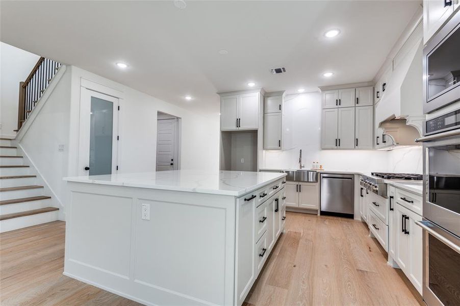 Kitchen featuring light wood-style flooring, recessed lighting, appliances with stainless steel finishes, light stone countertops, and white cabinets