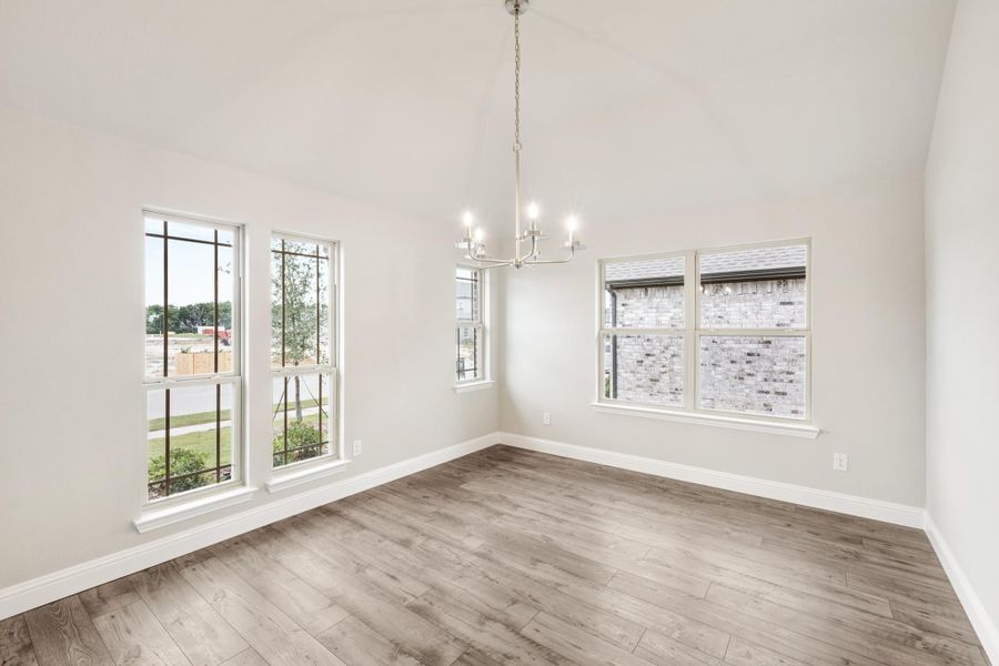 Empty dining room with vaulted ceiling, chandelier, hardwood floors, and multiple windows