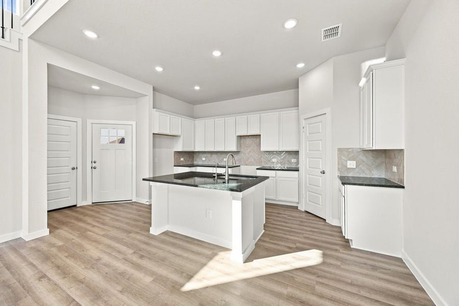 Kitchen with white cabinets, dark granite island, herringbone tile backsplash, and light wood floors