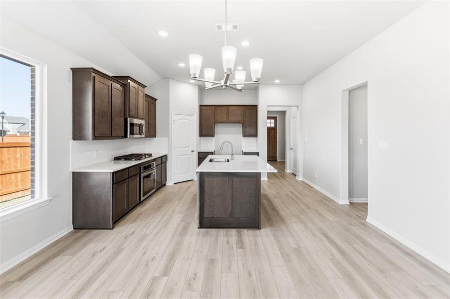 Kitchen featuring pendant lighting, a kitchen island with sink, dark brown cabinetry, light wood-style floors, and recessed lighting