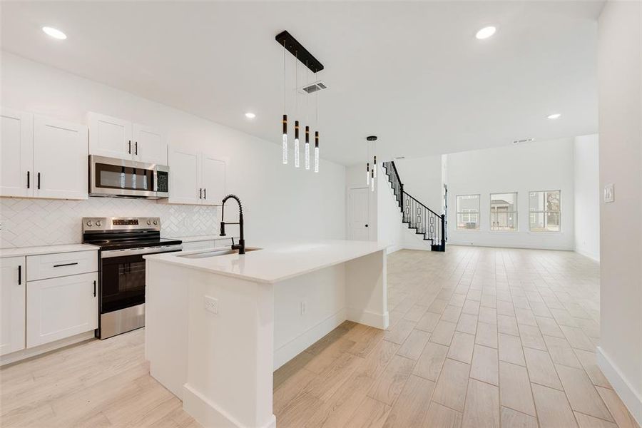 Kitchen with decorative light fixtures, a center island with sink, appliances with stainless steel finishes, white cabinets, and a sink