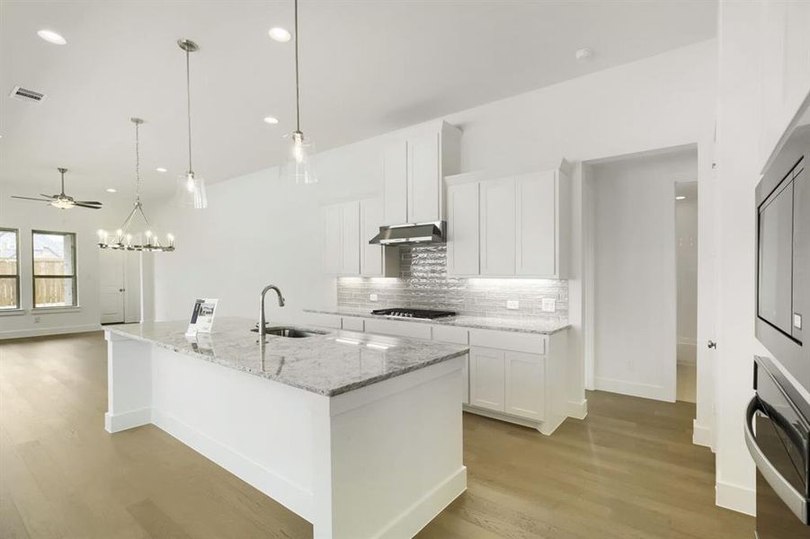 Spacious kitchen featuring a large island with sink, granite countertops, white cabinetry, a tiled backsplash, and recessed and pendant lighting