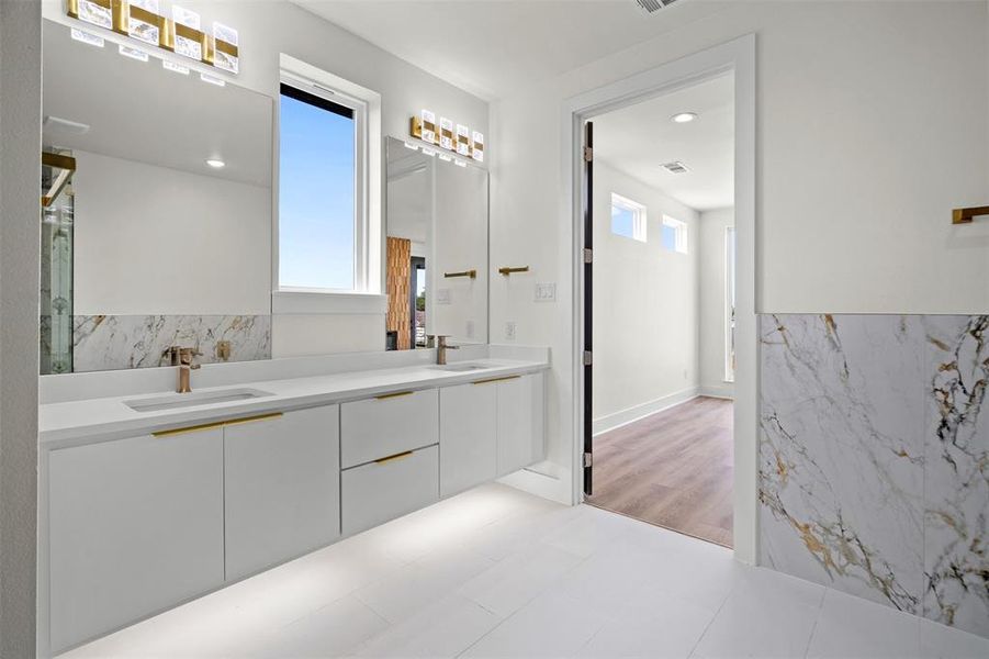 Modern bathroom featuring a long double vanity with white cabinets, gold hardware, and two sinks Modern bathroom featuring a long double vanity with white cabinets, gold hardware, and two sinks