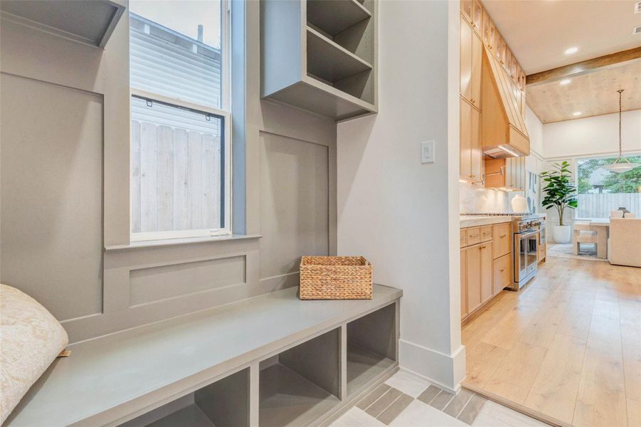 The mudroom features built-in cubbies, open shelving, and a long bench for convenient storage and organization. Designer tile flooring and detailed wall trim add sophistication to this practical space.