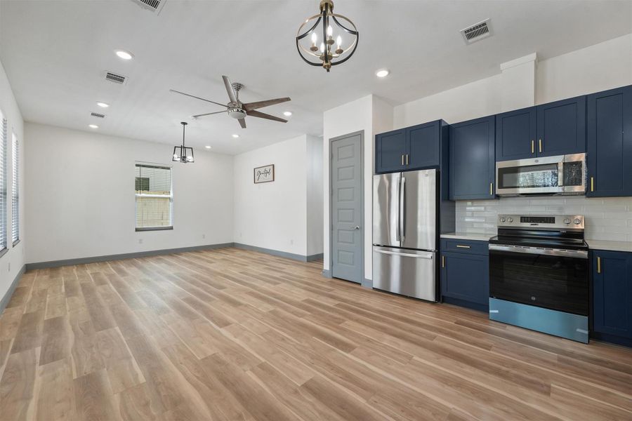 This modern, open-concept space features sleek, blue cabinetry, stainless steel appliances, and wood-look flooring. There's ample natural light, recessed lighting, and a ceiling fan for comfort. Perfect for entertaining or everyday living.