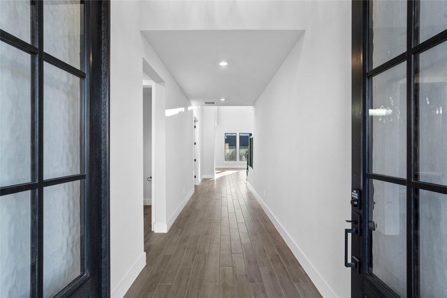 An inviting entrance opens up to an open-concept layout, seamlessly connecting the entry to the living areas with durable wood-look tile flooring and bright white walls with recessed lighting.