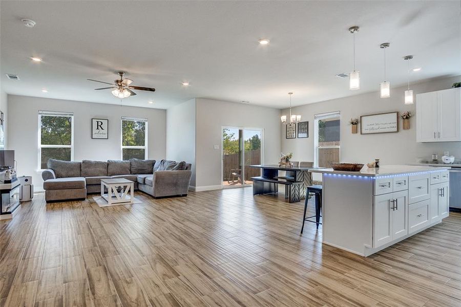 Kitchen featuring white cabinets, a breakfast bar, decorative light fixtures, ceiling fan, and open floor plan