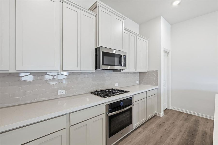 Kitchen featuring stainless steel appliances, tasteful backsplash, light wood-style floors, white cabinets, and light stone countertops