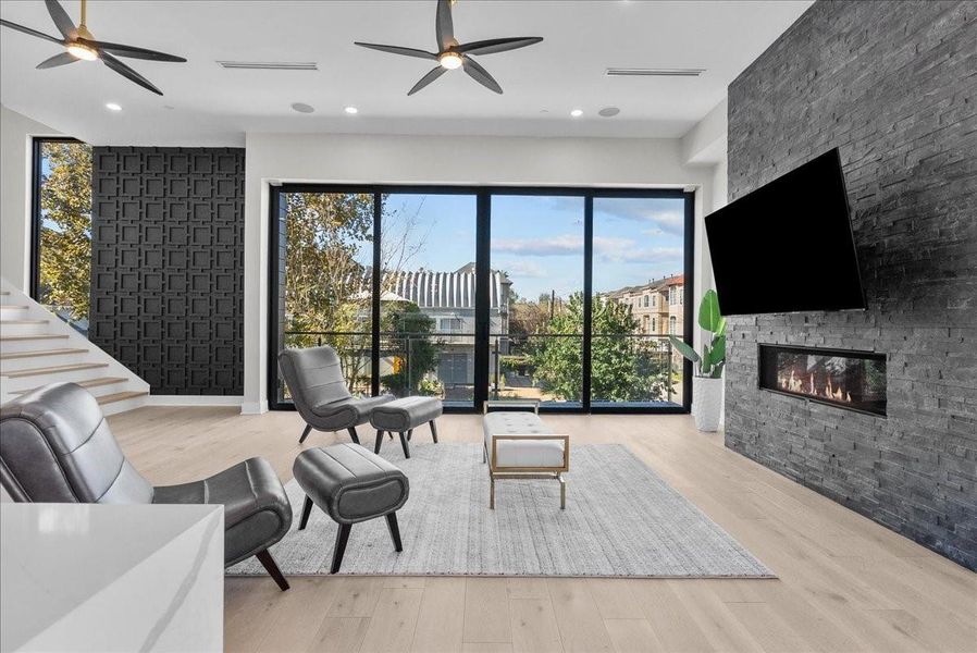 This modern living room features large floor-to-ceiling windows with a scenic view, a sleek black accent wall, and a cozy fireplace. The space is airy and bright, with stylish furnishings and contemporary ceiling fans, creating a perfect blend of comfort and elegance. This modern living room features large floor-to-ceiling windows with a scenic view, a sleek black accent wall, and a cozy fireplace. The space is airy and bright, with stylish furnishings and contemporary ceiling fans, creating a perfect blend of comfort and elegance.
