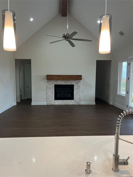 Unfurnished living room featuring high vaulted ceiling, a stone fireplace, ceiling fan, dark hardwood / wood-style floors, and beam ceiling