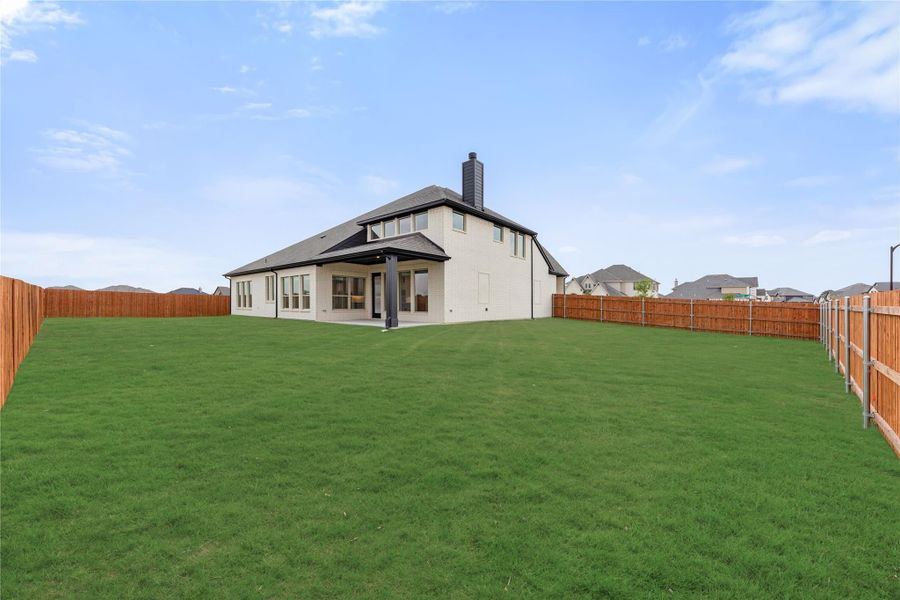 Rear view of two-story home with large fenced backyard, covered patio, and chimney