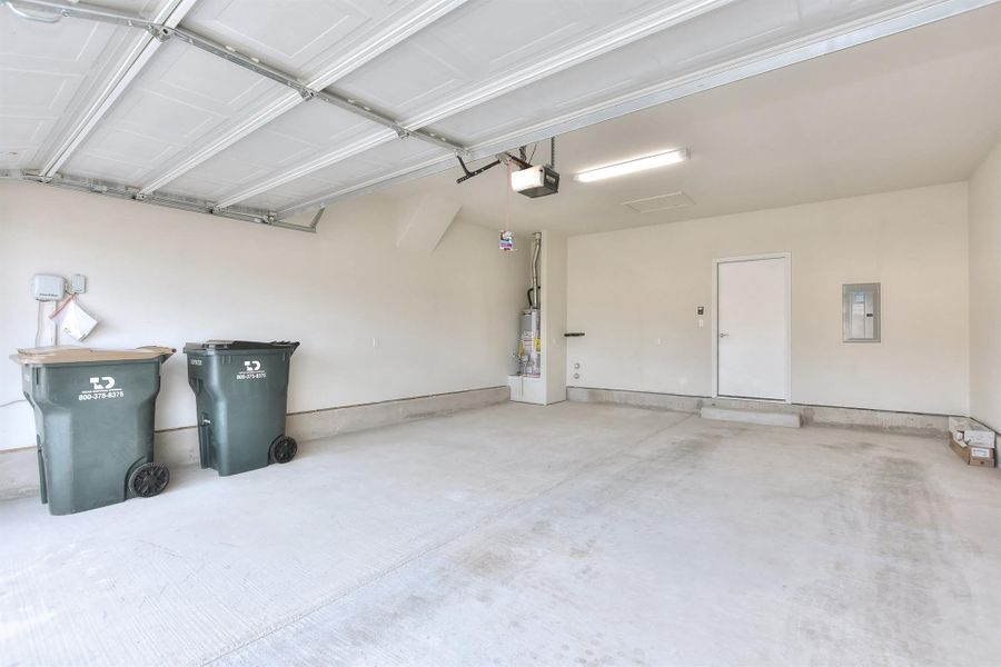 Garage with gas water heater, electric panel, and a garage door opener