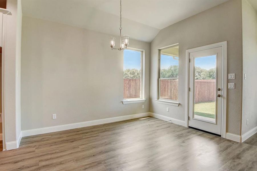 Unfurnished dining area featuring a chandelier, wood finished floors, lofted ceiling, and baseboards