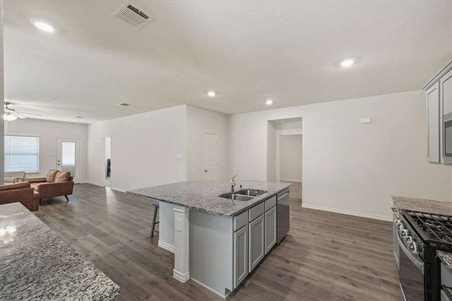 Kitchen featuring gray cabinets, open floor plan, light stone counters, dark wood-style floors, and an island with sink Kitchen featuring gray cabinets, open floor plan, light stone counters, dark wood-style floors, and an island with sink