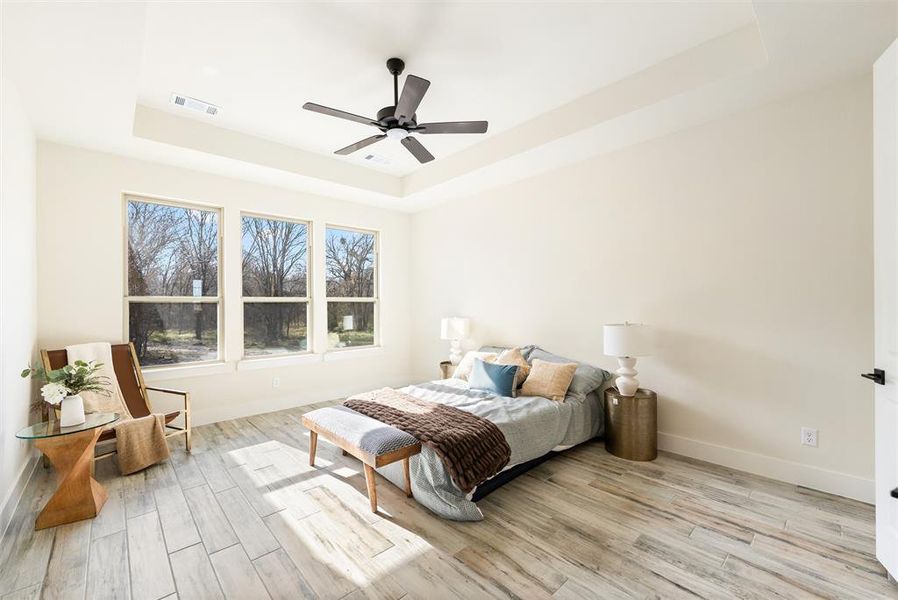Bedroom featuring a raised ceiling, light wood-style flooring, and ceiling fan
