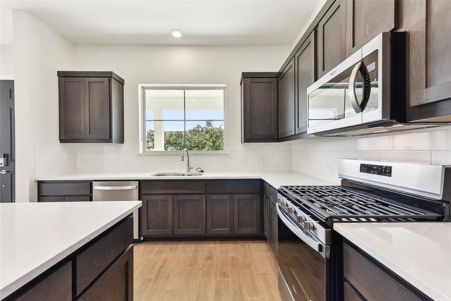 Kitchen with appliances with stainless steel finishes, light wood finished floors, a sink, and dark brown cabinets Kitchen with appliances with stainless steel finishes, light wood finished floors, a sink, and dark brown cabinets