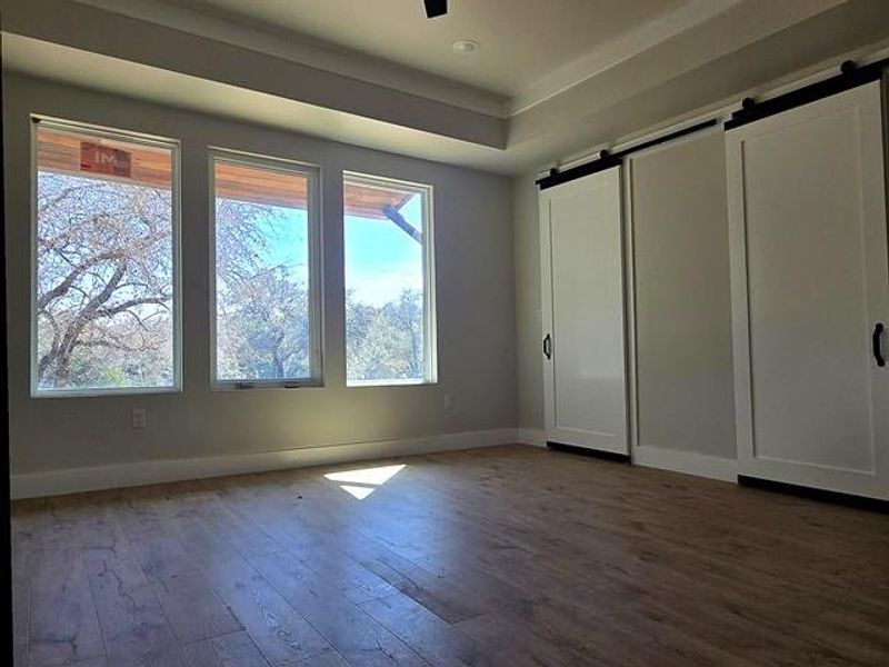 Unfurnished bedroom featuring a barn door, dark wood finished floors, ceiling fan, and a raised ceiling