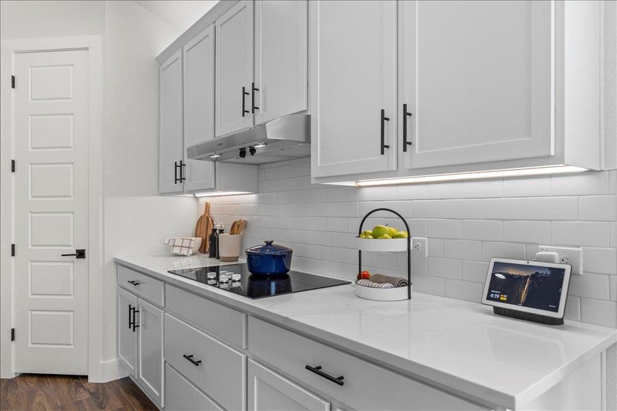 Kitchen featuring backsplash, dark wood finished floors, under cabinet range hood, white cabinetry, and black electric stovetop