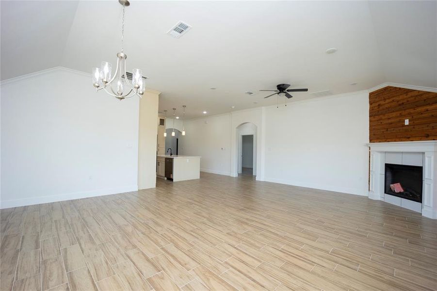 Unfurnished living room featuring vaulted ceiling, a fireplace, ornamental molding, light wood finished floors, and a chandelier
