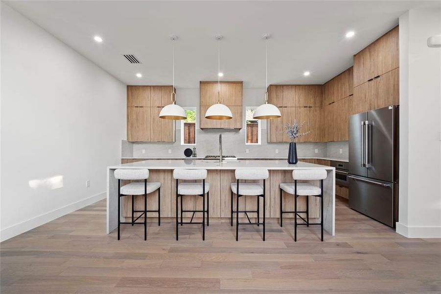 Kitchen with a kitchen island with sink, decorative light fixtures, backsplash, light wood-type flooring, and high end refrigerator