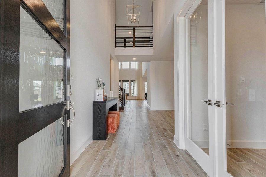 Modern, bright entryway with a sleek wood floor, high ceiling, and contemporary lighting. The open layout leads to a spacious living area, and glass double doors add elegance and openness. Modern, bright entryway with a sleek wood floor, high ceiling, and contemporary lighting. The open layout leads to a spacious living area, and glass double doors add elegance and openness.