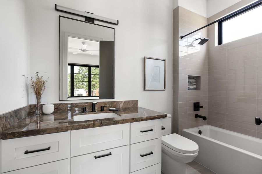 The private secondary bathroom for bedroom #1 is finished with a stone topped vanity, modern lighting, a tub and shower combination with tile surround, black fixtures, a built-in shower Niche and a transom window for added natural light. Large walk in closet as well.