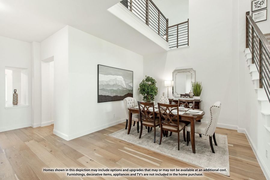 Dining room with two-story ceiling, wood floors, dark wood table, and open staircase railing above