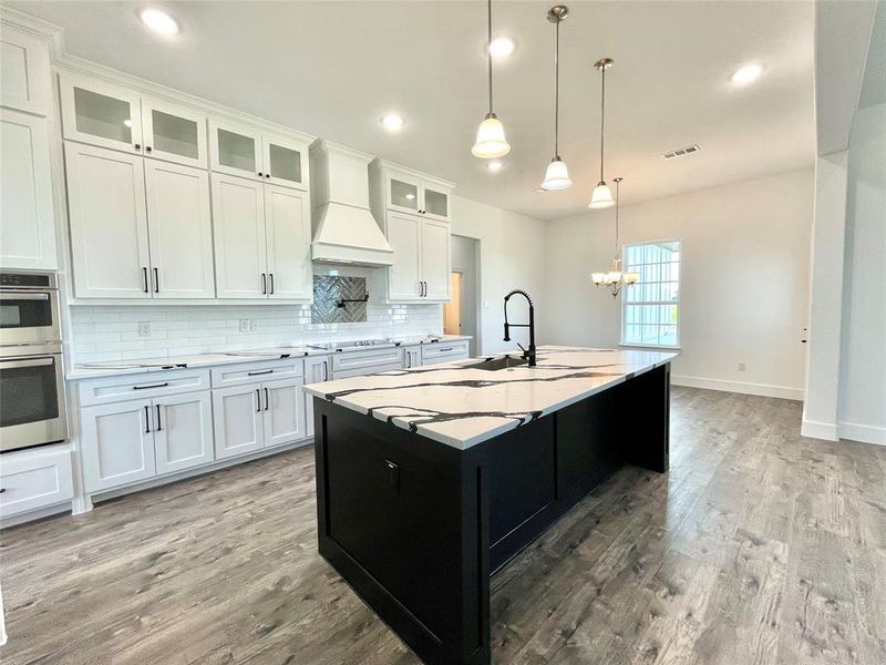 Kitchen with stainless steel double oven, custom range hood, backsplash, a notable chandelier, and visible vents Kitchen with stainless steel double oven, custom range hood, backsplash, a notable chandelier, and visible vents