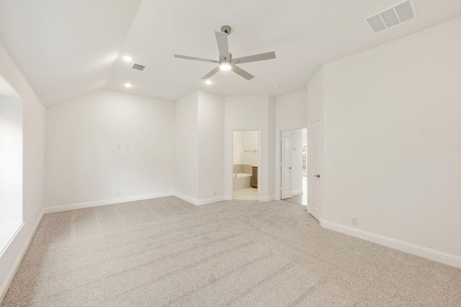 Empty bedroom with vaulted ceiling, ceiling fan, carpet flooring, and ensuite bathroom doorway