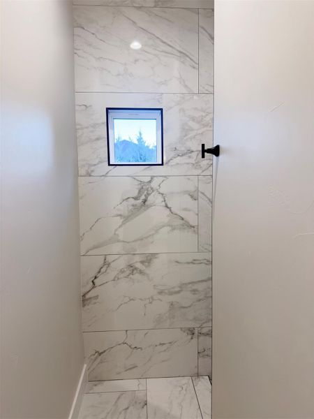 Floor-to-ceiling marble-patterned tile wraps this modern walk-in shower featuring a high square window. Floor-to-ceiling marble-patterned tile wraps this modern walk-in shower featuring a high square window.