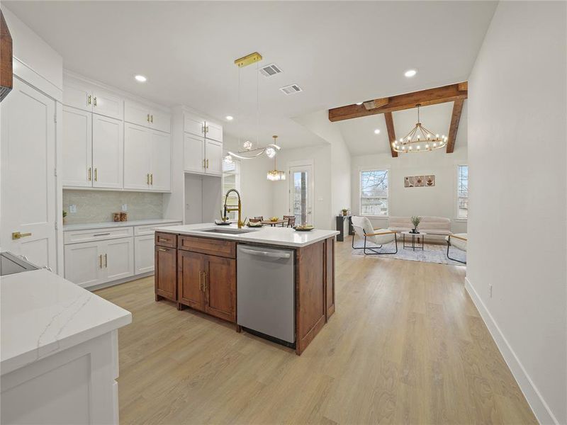 Kitchen featuring two tone color scheme, stainless steel dishwasher, light wood-style flooring, a center island with sink, and suspended lighting