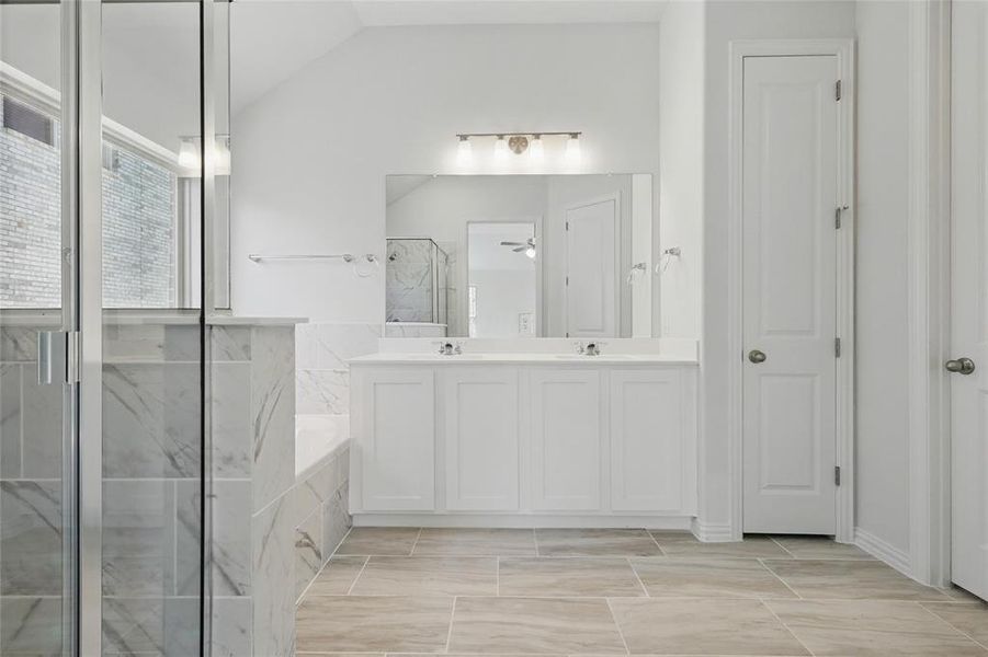 Bathroom featuring lofted ceiling, a garden tub, a sink, a marble finish shower, and double vanity