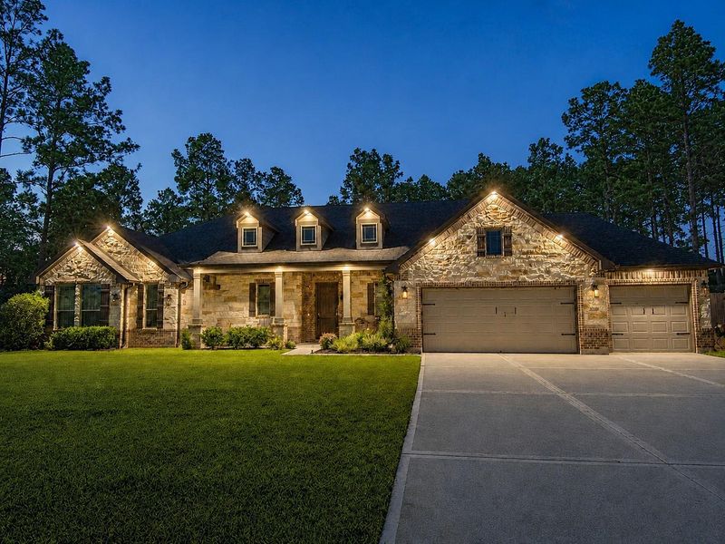 Beautiful evening view showcasing the home’s upgraded exterior puck lighting, highlighting the architectural details and creating impressive nighttime curb appeal.