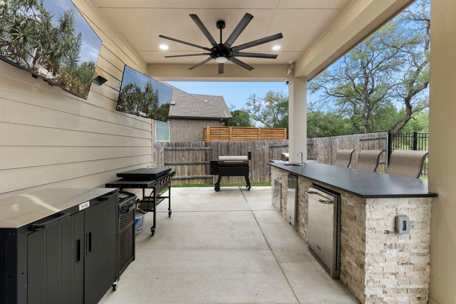 Covered outdoor living space featuring dual wall-mounted televisions and a ceiling fan