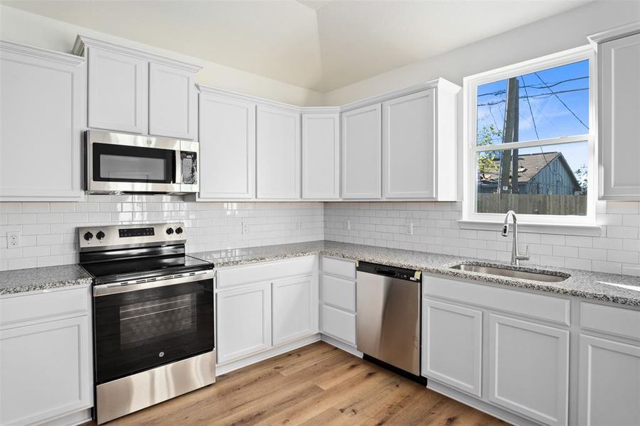 Kitchen featuring stainless steel appliances, backsplash, granite countertops, and white cabinets Kitchen featuring stainless steel appliances, backsplash, granite countertops, and white cabinets